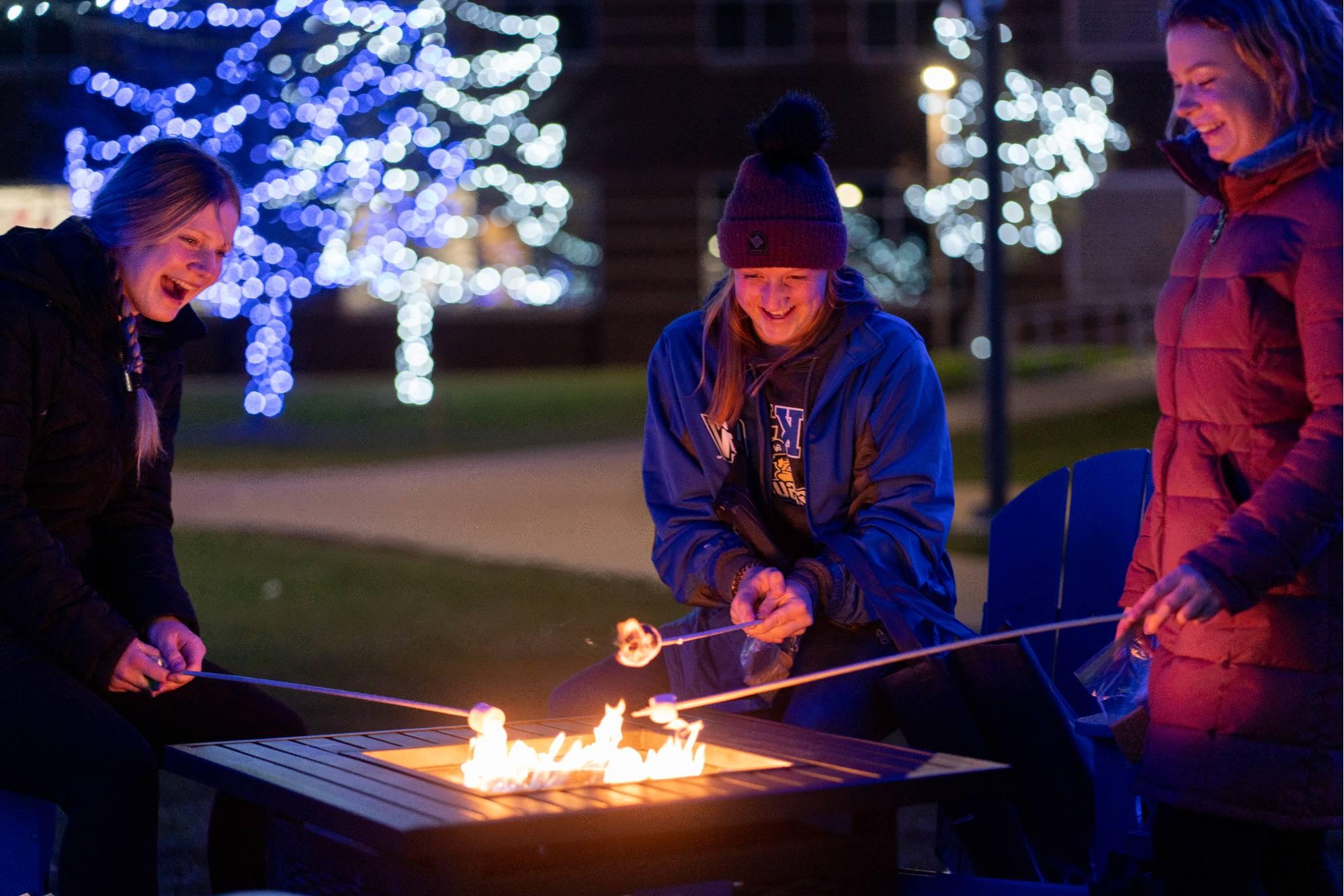 Group of students standing outside gathered around a fire roasting s'mores.